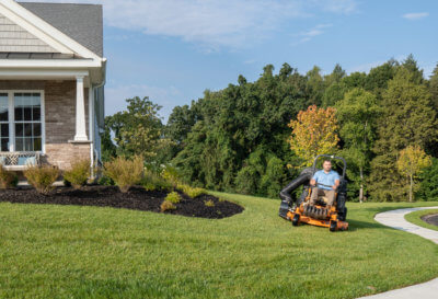 Man mowing lawn on an orange riding mower on a slight incline