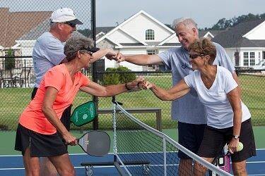 Two active adult couples fist bumping over pickle ball net