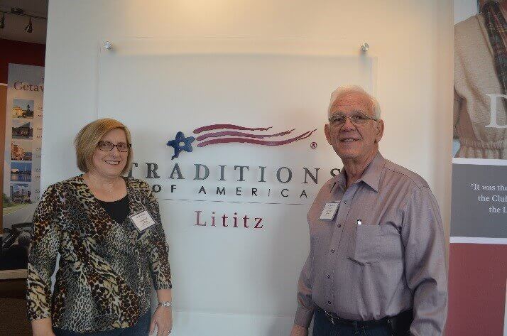 Two people standing in front of a Traditions of America Lititz sign