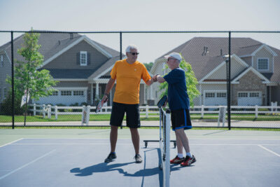 Two active adults shaking hands across the net on a tennis court