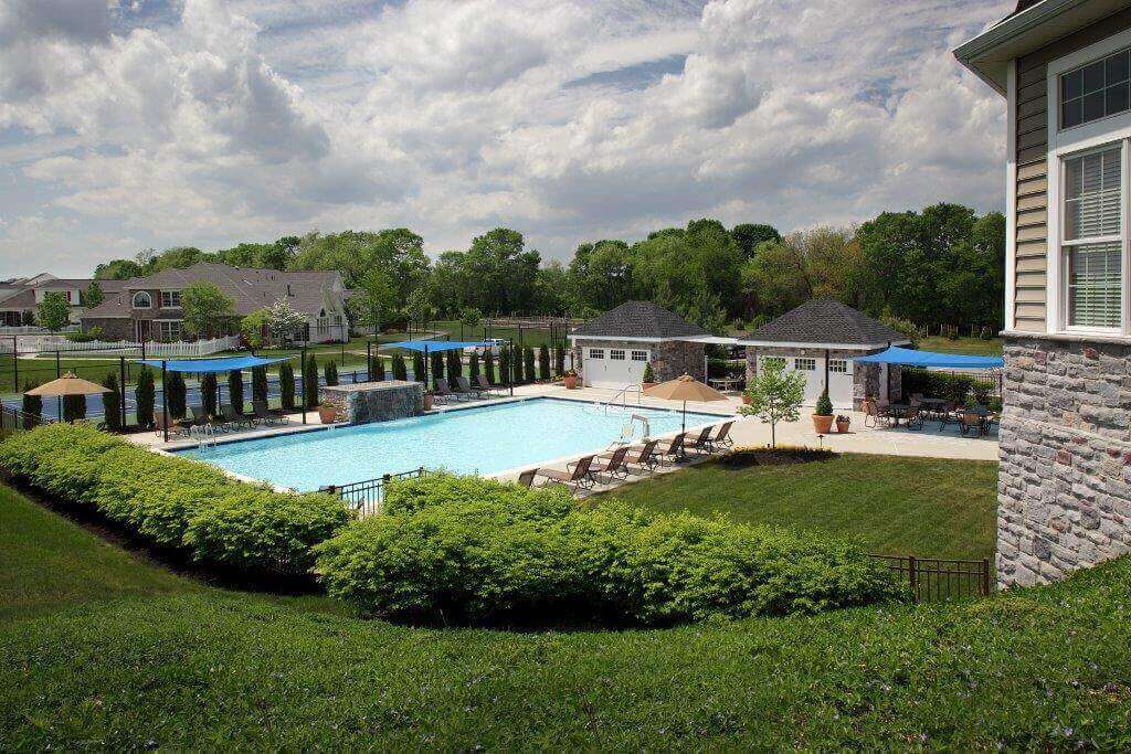 Large pool surrounded by lounge chairs with a tennis court in the background
